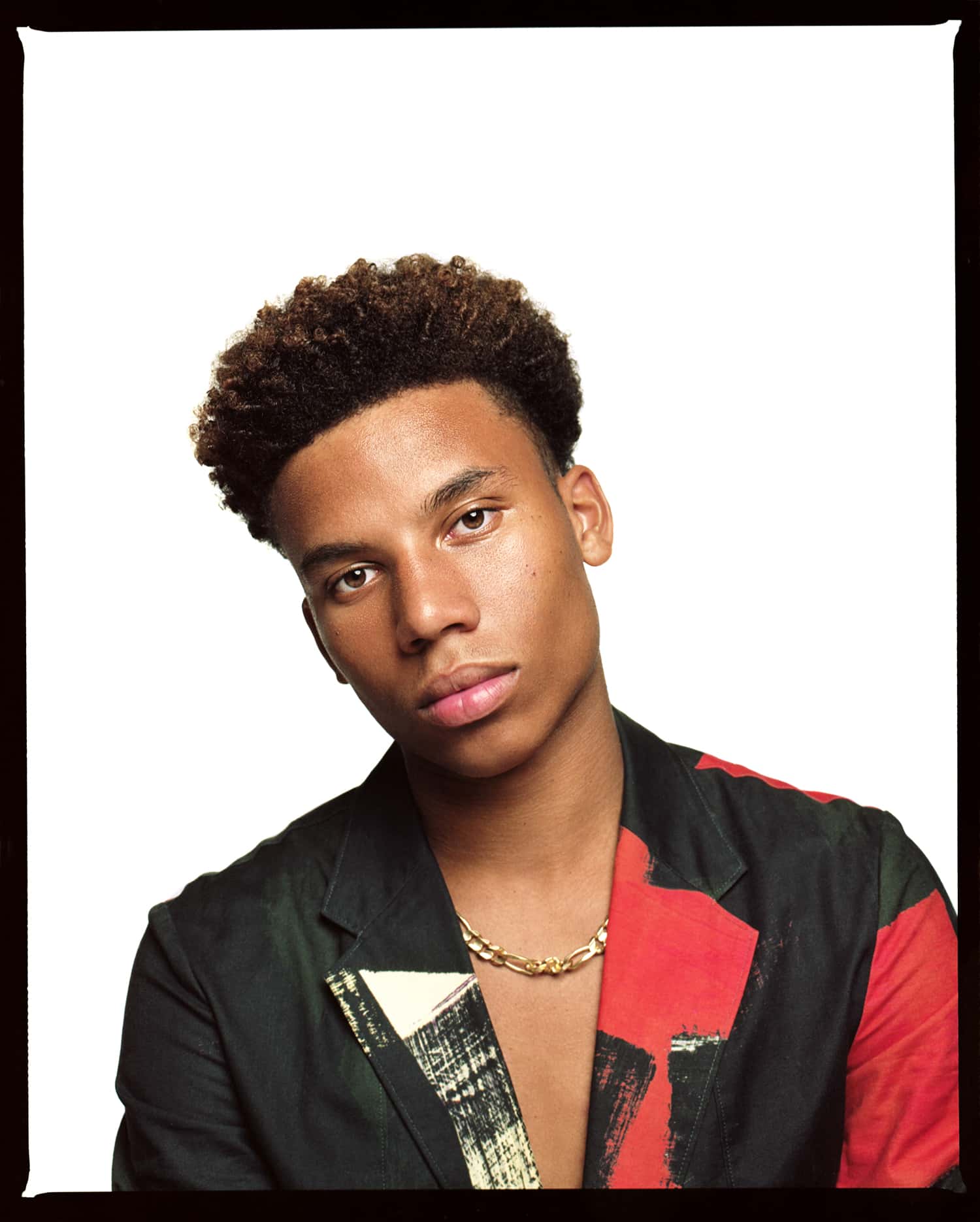 Color photograph shot on the Mamiya RZ67 camera with Kodak Portra film, featuring model and grandson of Bob Marley, Saiyan Marley. He is wearing a colorful red, black and yellow suit and a gold necklace. Studio photo shoot with a white backdrop. Photographed by fashion, beauty and portrait photographer Maria Bruun in New York City.